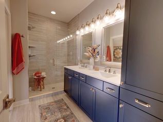 Bright bathroom with blue cabinets, double sinks, large mirror lights, and a tiled shower/tub area.