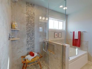 Modern bathroom with glass shower, tiled wall, and white tub with red towel