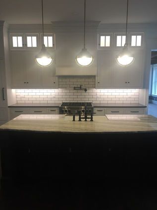Modern kitchen with large island, white tile backsplash, and pendant lights hanging above.
