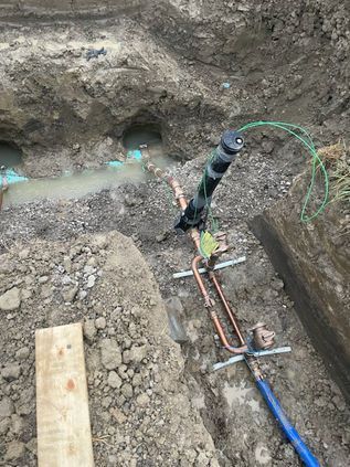 Trench excavation with exposed pipes and cables, including blue and orange utility lines in muddy soil