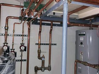 Boiler room with copper pipes, gauges, valves, and a gray water heater on the right.