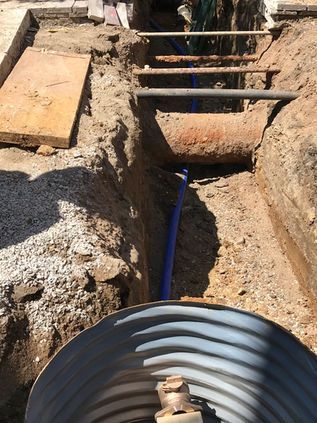 Trenched construction site with a blue pipe and concrete culvert under a dirt path