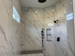 Modern tiled walk-in shower with glass opening, black fixtures, and recessed shelf.