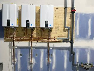 Three white wall-mounted water heaters with copper pipes in a utility room