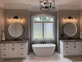 Elegant bathroom with twin vanities, round mirrors, and a freestanding tub beneath a window