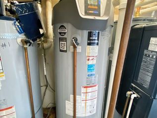 Water heater in a utility closet beside pipes and a black tank.