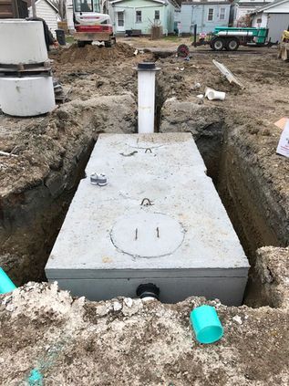 Concrete septic tank lid in a dug-out construction site with pipes and muddy ground