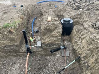 Backyard utility trench with black and blue pipes, gravel, and a black septic tank under construction
