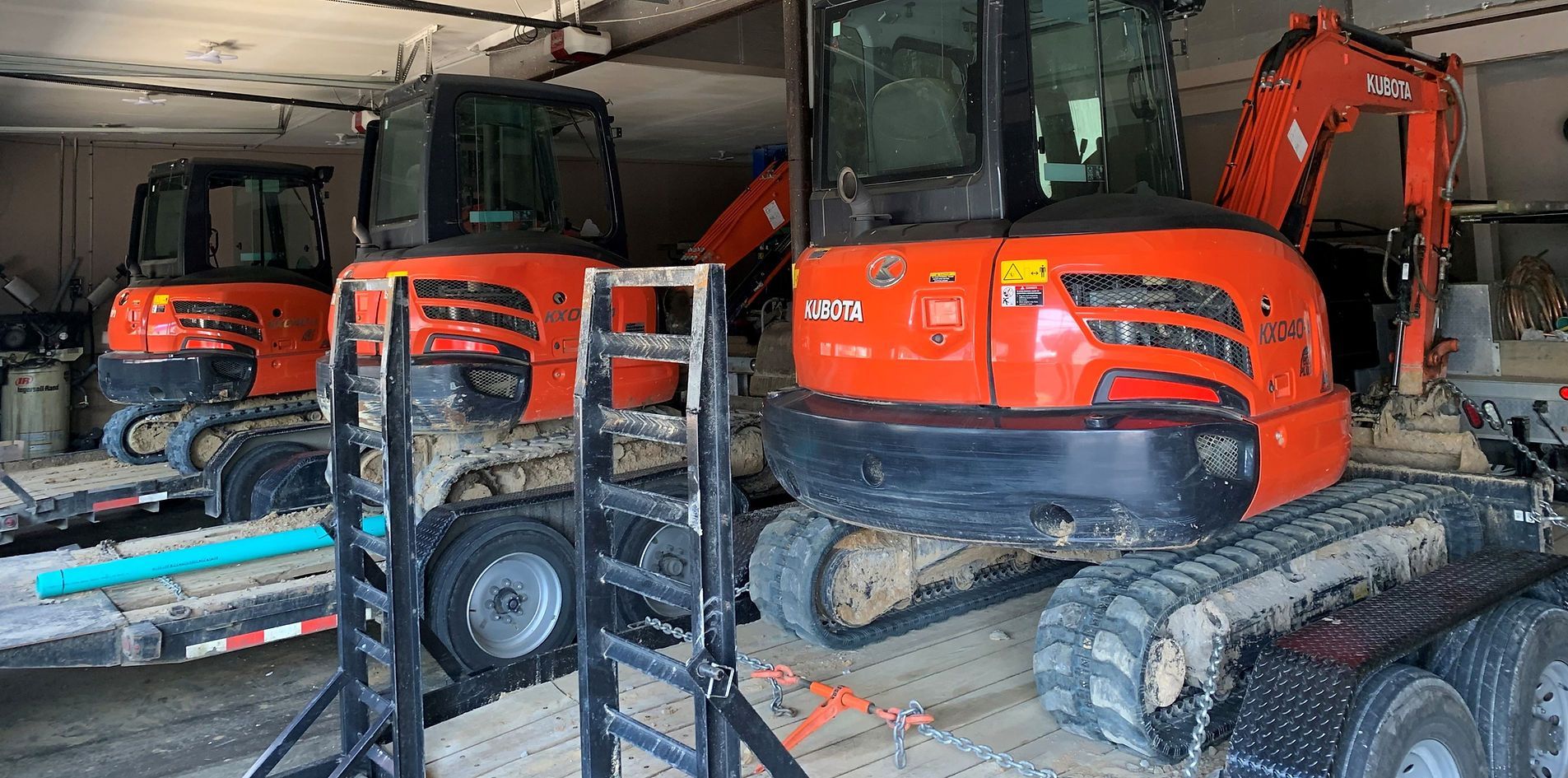 Orange excavators parked inside a garage, with a small forklift in the foreground.