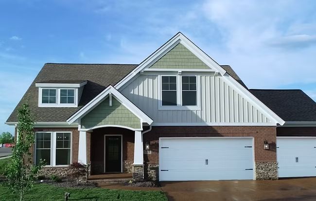 Suburban house with brick and gray siding, white garage door, and wet driveway under a blue sky