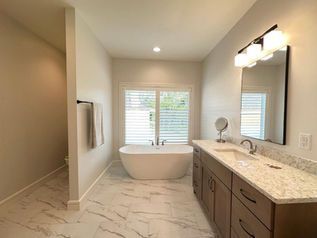Modern bathroom with a freestanding tub, double vanity, marble floor, and window blinds