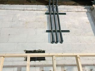 Exposed black conduit pipes on a white wall above unfinished wooden framing