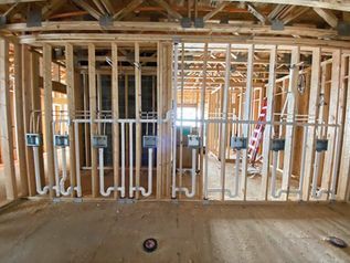Interior of a house under construction with exposed wooden framing and plumbing pipes.
