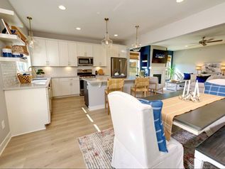 Bright open-plan kitchen and dining area with white cabinets, wood floors, and modern furniture