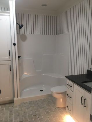Bathroom with white shower tub, striped wall paneling, toilet, and vanity with black countertop.