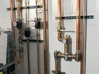 Pipes and gauges mounted on a tiled wall in a utility room