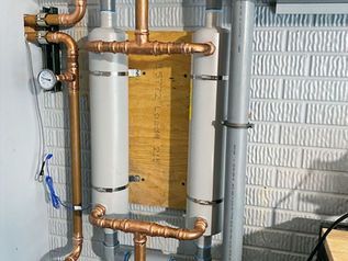 Copper and white PVC pipes with a gauge mounted on a brick exterior wall