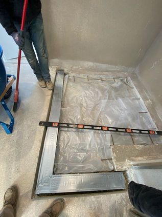 Workers measuring a gray tiled floor area with a level and tape in a narrow room
