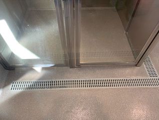 Metal elevator doors with a vented floor threshold and bright light reflection on the wall