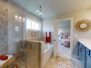 Modern bathroom with glass shower, freestanding tub, and red towels visible through an open doorway