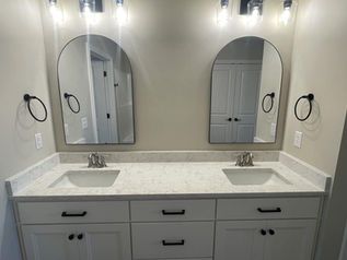Double vanity bathroom with gray cabinets, two mirrors, and wall sconces above a marble countertop.
