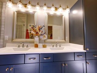 Blue bathroom vanity with double mirrors, bright lights, and flowers on the counter
