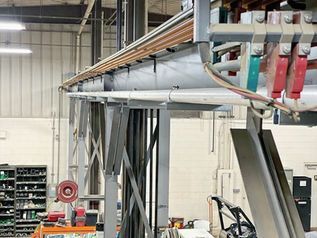 Industrial workshop with overhead piping, machinery, and a forklift in a warehouse interior