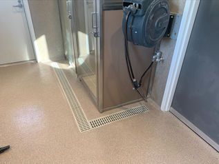 Industrial room with tan flooring, metal cabinet, and floor drain grate near a wall.