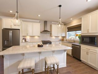 Bright modern white kitchen with island, stainless appliances, and two stools
