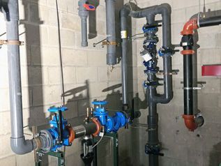 Industrial piping and valves on a basement wall, with blue and red pipes and a pump assembly.