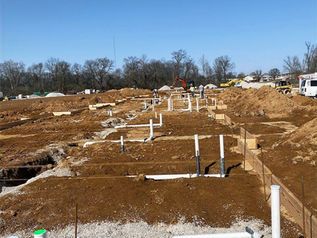 Excavation site with trenches and white pipes in a dirt lot under a clear blue sky