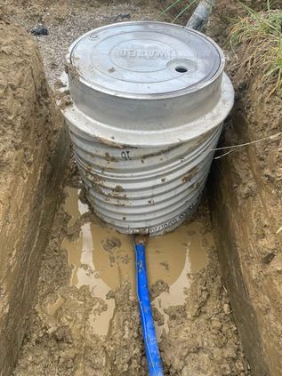 Round utility tank in a muddy trench with a blue pipe connected at the bottom
