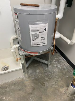 Gray water heater or tank on a stand in a utility room with pipes and concrete floor