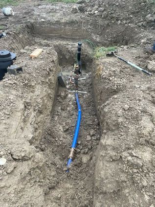 Trench with exposed blue pipe and concrete utility box in a dirt excavation site