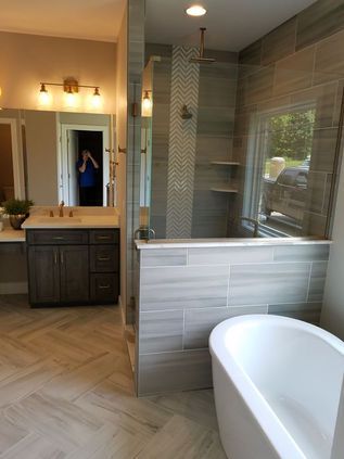 Modern bathroom with freestanding tub, glass shower, dark vanity, and herringbone tile flooring