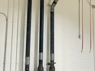 Three black utility pipes with metal joints against a white brick wall.