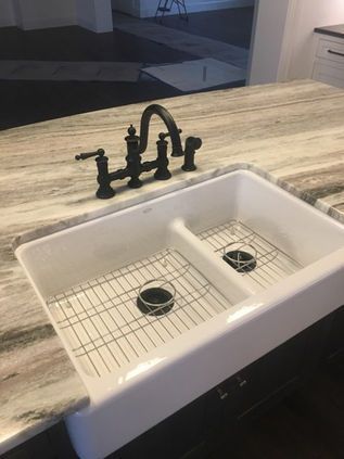 White farmhouse sink with black faucet and granite countertop in a kitchen, seen from above.