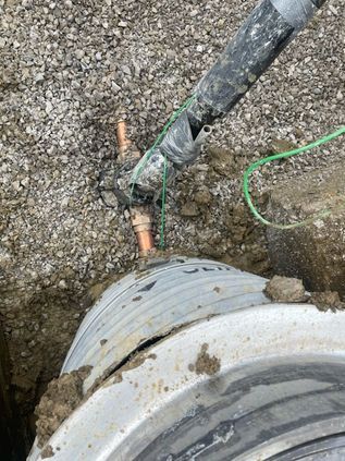 Broken pipe and exposed copper wire in muddy ground near a large pipe joint