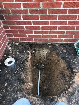 Backyard corner with a large dug-up hole beside a brick wall and scattered soil debris