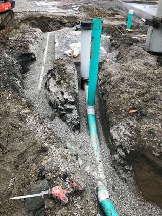 Trenched ground with exposed teal pipes and white conduit at a construction site