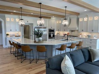Bright modern kitchen with large island, white cabinets, pendant lights, and blue sofa in foreground