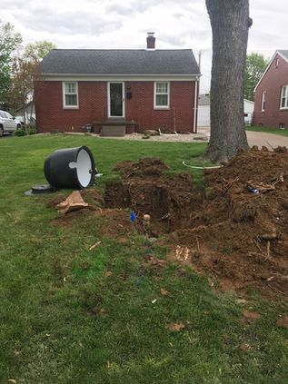 Backyard with a large uprooted tree, soil pile, and a fallen black-and-white barrel near a red house