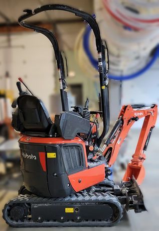 Small orange-and-black compact excavator with tracks and raised arm in an indoor workspace