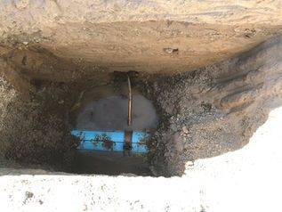 Small underground pit with a blue object and a metal pipe or rod in the center