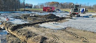 Construction site with excavator, gravel piles, and muddy road under a clear blue sky