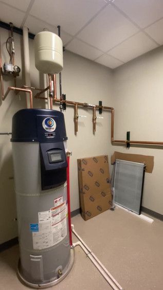 Utility room with a tall gray water heater, copper pipes, and a small white expansion tank on the wall.