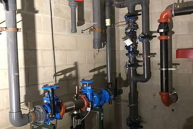 Industrial piping and valves in a mechanical room, with blue and red components on a concrete wall