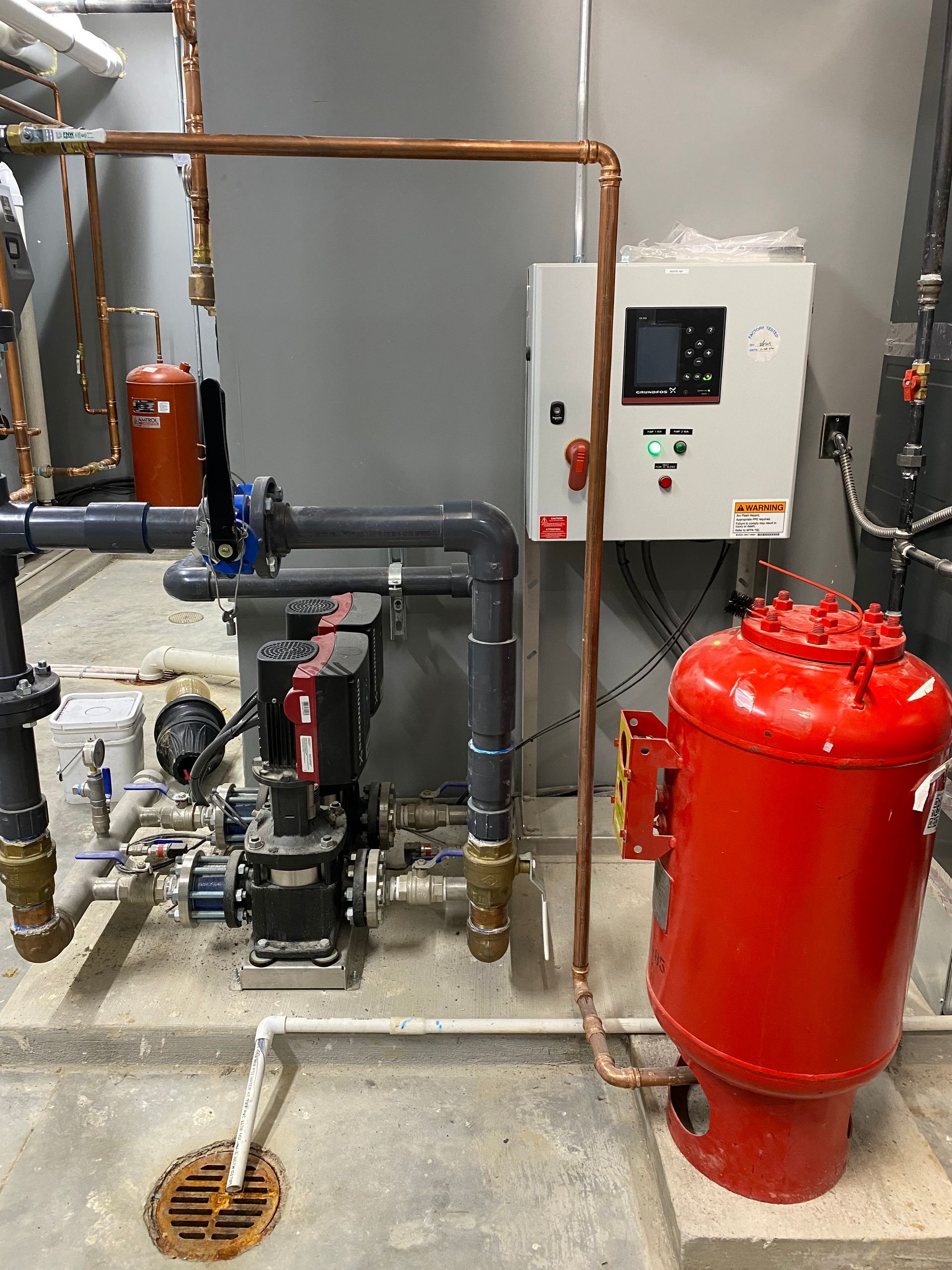 Industrial boiler room with red pressure tank, pipes, pump, and control panel on a concrete floor