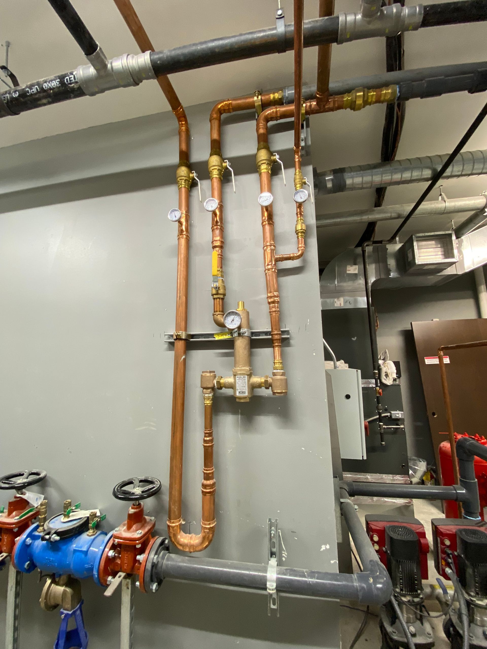 Copper and gray industrial pipes with valves and gauges in a utility room