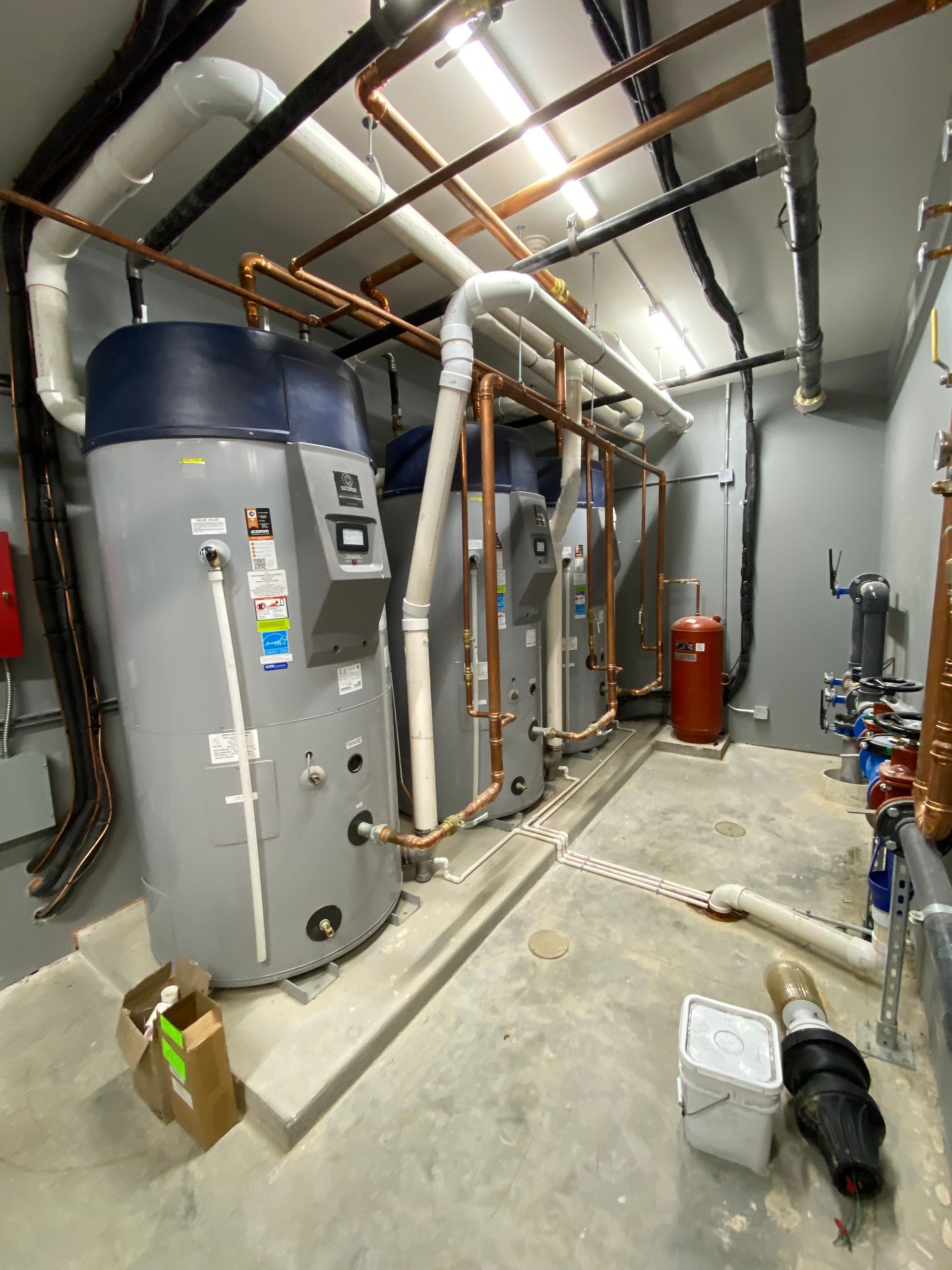 Boiler room with large gray tank, copper pipes, insulated ducts, and industrial equipment on concrete floor